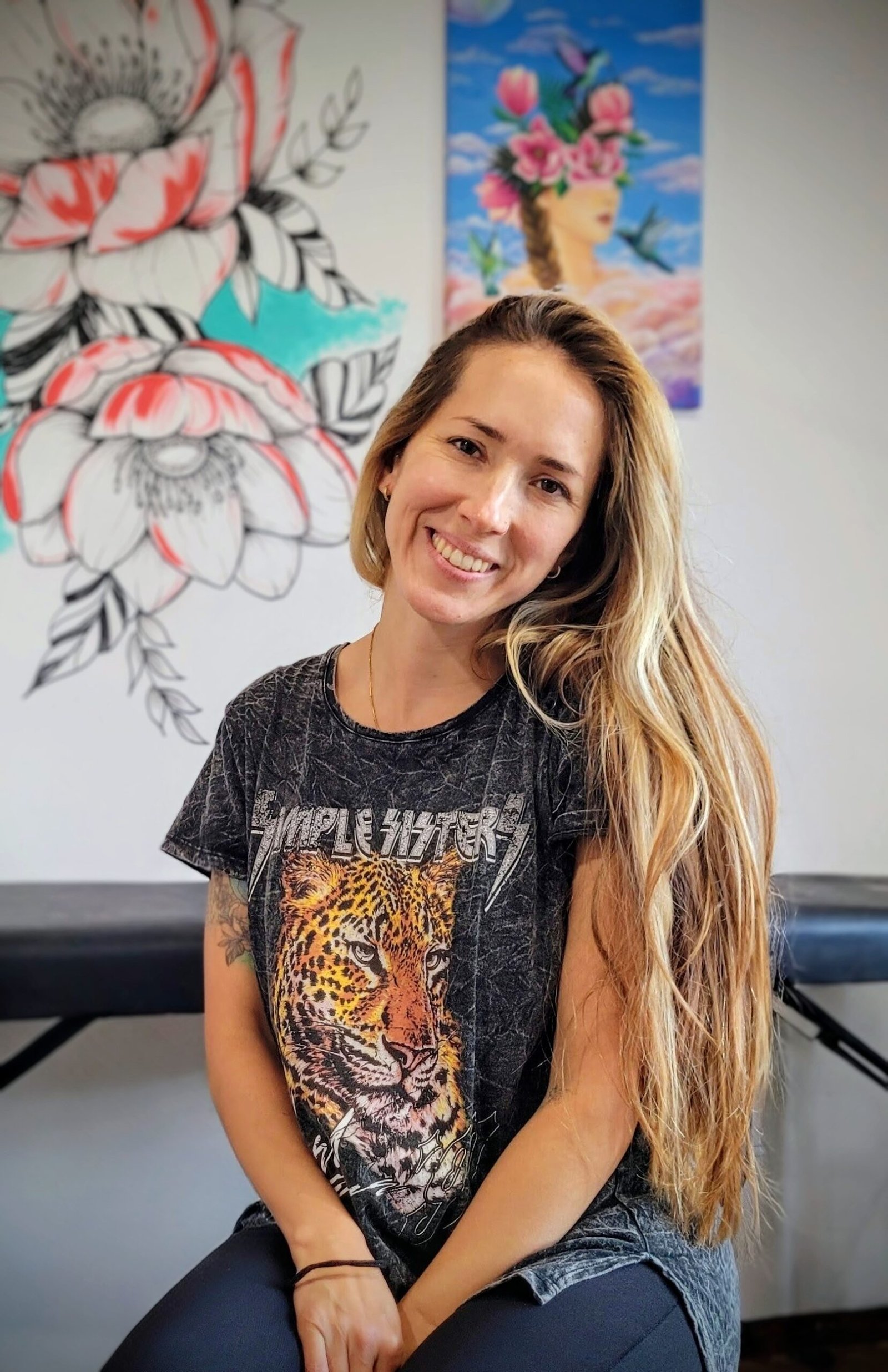 Dafne Aguilar, artista de Tres Algarrobos, Buenos Aires, posando junto a su mural floral pintado a mano y una obra enmarcada con elementos naturales y oníricos.